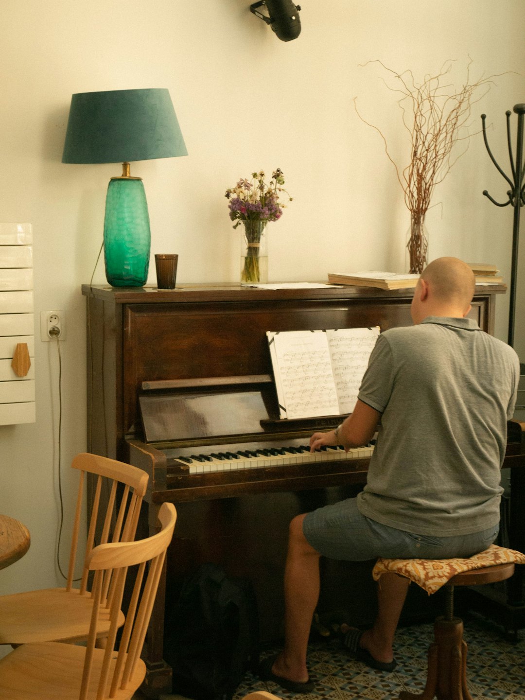 A bald person plays an upright piano in a room.