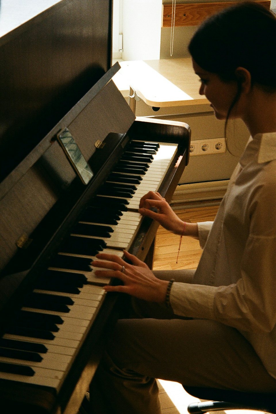 Young woman plays piano with smartphone on stand.